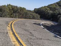 a motorcycle going down a winding hill road next to trees and a blue sky in the background