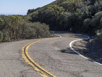 a motorcycle going down a winding hill road next to trees and a blue sky in the background