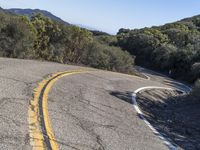 a motorcycle going down a winding hill road next to trees and a blue sky in the background