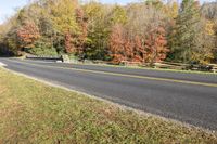 an empty paved road with multiple trees around it next to a grass and wooden fence