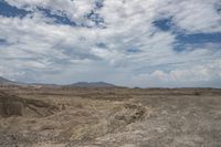 a large open desert with some hills in the background and clouds overhead as well as some mountains are visible in the distance