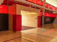 a empty gym has a basketball court and lockers with red and black doors and wood flooring