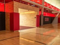 a empty gym has a basketball court and lockers with red and black doors and wood flooring