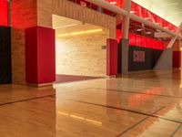 a empty gym has a basketball court and lockers with red and black doors and wood flooring