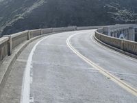 a motorcycle is driving along the curved road over a bridge in a valley on a sunny day