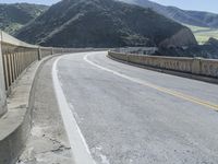 a motorcycle is driving along the curved road over a bridge in a valley on a sunny day