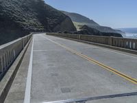 a motorcycle is driving along the curved road over a bridge in a valley on a sunny day