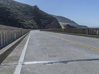 a motorcycle is driving along the curved road over a bridge in a valley on a sunny day