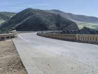 a motorcycle is driving along the curved road over a bridge in a valley on a sunny day