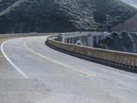 a motorcycle is driving along the curved road over a bridge in a valley on a sunny day