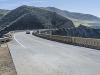 a motorcycle is driving along the curved road over a bridge in a valley on a sunny day