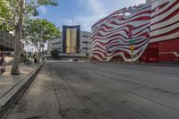 the sidewalk is empty and next to the building that's next to it has a red and white striped design on it