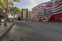 the sidewalk is empty and next to the building that's next to it has a red and white striped design on it