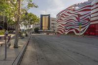 the sidewalk is empty and next to the building that's next to it has a red and white striped design on it