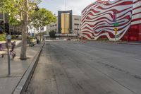 the sidewalk is empty and next to the building that's next to it has a red and white striped design on it