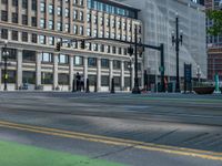 the green paint is painted on a bike path in front of an office building and large, trees