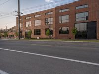 an empty street in front of a large red brick building on the other side of the road is a street light that has a line for motorists