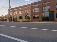 an empty street in front of a large red brick building on the other side of the road is a street light that has a line for motorists