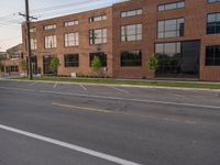 an empty street in front of a large red brick building on the other side of the road is a street light that has a line for motorists