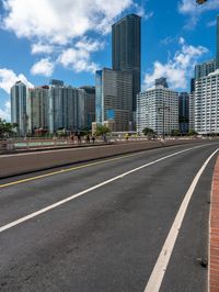 a very wide road next to a very tall building near the water with people walking on it