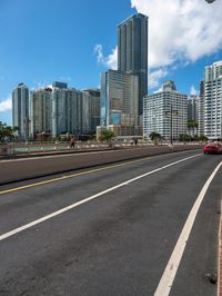 a very wide road next to a very tall building near the water with people walking on it