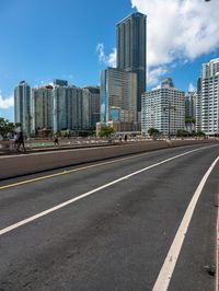 a very wide road next to a very tall building near the water with people walking on it