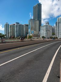 a very wide road next to a very tall building near the water with people walking on it