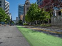 the green paint is painted on a bike path in front of an office building and large, trees