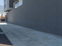 a sidewalk with building and orange fire hydrant near it on a sunny day with mountains in the background