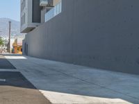 a sidewalk with building and orange fire hydrant near it on a sunny day with mountains in the background