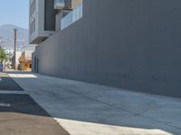 a sidewalk with building and orange fire hydrant near it on a sunny day with mountains in the background