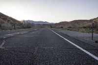 an empty country road with no cars on it at sunrise with mountains in the distance