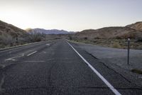 an empty country road with no cars on it at sunrise with mountains in the distance