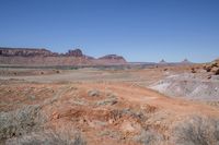 a dirt road through a desert plain with a mountain behind it and a clear blue sky in the background