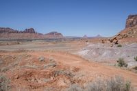 a dirt road through a desert plain with a mountain behind it and a clear blue sky in the background