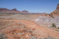 a dirt road through a desert plain with a mountain behind it and a clear blue sky in the background