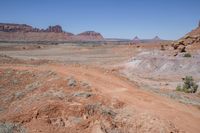 a dirt road through a desert plain with a mountain behind it and a clear blue sky in the background