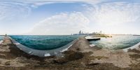 a fisheye view of a body of water near a pier with a city skyline in the background