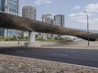 an overpass above the street with lots of people riding bicycles on it, some with buildings in the background