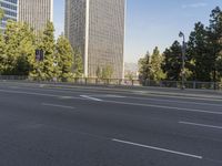 empty highway near skyscrapers with green trees in foreground and sky in the background