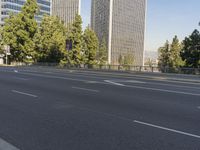 empty highway near skyscrapers with green trees in foreground and sky in the background