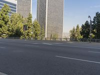 empty highway near skyscrapers with green trees in foreground and sky in the background