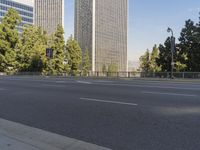 empty highway near skyscrapers with green trees in foreground and sky in the background