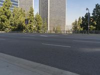 empty highway near skyscrapers with green trees in foreground and sky in the background