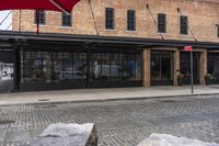 large red umbrella sitting outside of a restaurant front with stone benches in the sidewalk next to the sidewalk