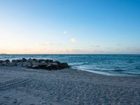 there are rocks and surfboards in the sand on a beach at dusk overlooking the sea