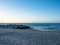 there are rocks and surfboards in the sand on a beach at dusk overlooking the sea