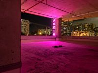 a rooftop parking garage with a bright neon sign above the garage floor, below an inner parking garage in a modern city with high rise to the skyscrapers