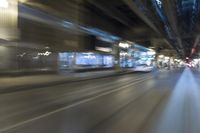 a blurry image of a train moving down a city street at night, with a bus turning the right