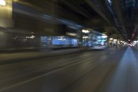 a blurry image of a train moving down a city street at night, with a bus turning the right